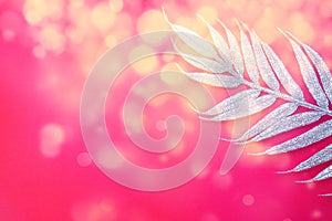 Artificial festive exotic silver branch with long leaves on a bright pink or red background. Copy space. Flat lay. Free