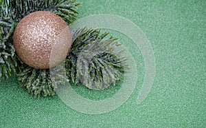 Artificial fir branch with golden shiny Christmas ball on a green glitter background. Copy space