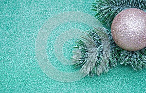 Artificial fir branch with golden shiny Christmas ball on a green glitter background. Copy space