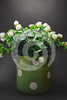 Artificial flowers in a green pot on a gray background illuminated from above. Beautiful dark background with green and white flow