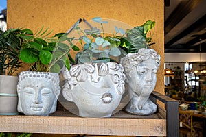 Artificial flowers in stone vases in form of heads of idols on a shelf as an interior decoration