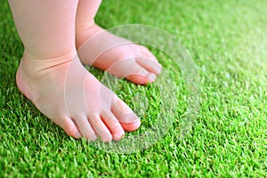 Artificial grass background. Tender foots of a baby on a green artificial turf.