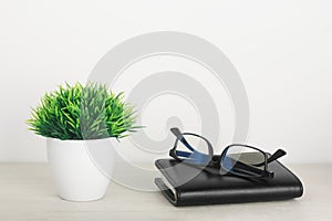 Artificial grass in a pot with glasses and notepad on a wooden table on a white background