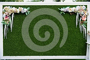 artificial grass wedding backdrop in a white frame decorated with flowers