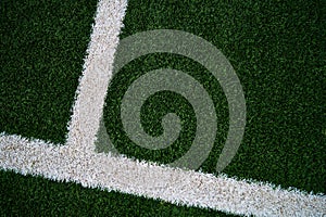 Artificial green grass with darker edges and with white up-side down shifted T to the far left