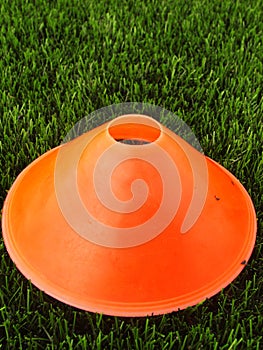 Artificial green plastic grass in background with bright orange plastic cone. Mark on winter footbal playground.