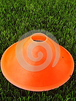 Artificial green plastic grass in background with bright orange plastic cone. Mark on winter footbal playground. photo