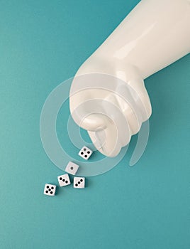 Artificial hand throwing dice on a teal background.