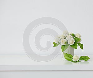 The artificial jasmine flower in the pot at the white table with the white wall background