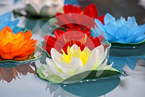 Artificial lotus flowers in various colors floating on the water surface with beautiful reflection.