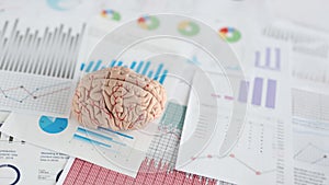 Artificial model of human brain lying on documents with graphs closeup
