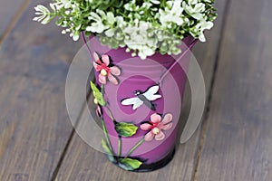 Artificial part of a green bush in a pink bucket with flowers and a butterfly on a wooden floor