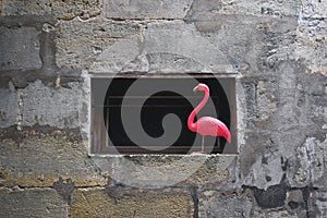 Artificial pink flamingo used as a decoration on the window. Surrounded by stone wall. Dada concept, background