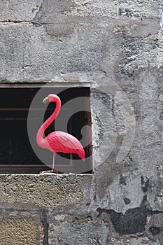 Artificial pink flamingo used as a decoration on the window. Surrounded by stone wall. Dada concept, background