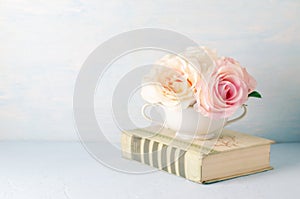 Artificial pink rose flowers with vintage book on blue background