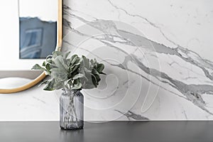 Artificial plant in glass vase compose with gold stainless mirror frame on gray spray-painted  working table with  marble wall in
