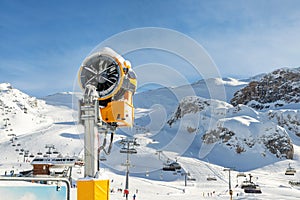 Artificial Snow cannon near piste.Ski lift ropeway on hilghland alpine mountain winter resort on bright sunny day