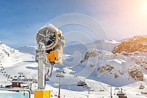 Artificial Snow cannon near piste.Ski lift ropeway on hilghland alpine mountain winter resort on bright sunny day. panoramic wide