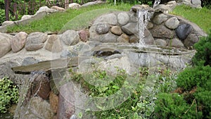 An artificial waterfall made of stones and water against a background of green vegetation. Water flows into the pond