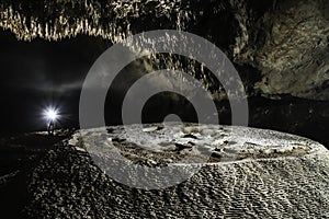 Artificially highlighted limestone formations in a cave with a speleologist in the background