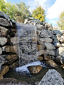 an artificialwaterfall in a park against the backdrop of a stone wall