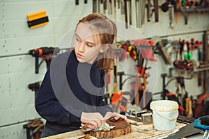 Artisan boy is putting a protective mordant on the wood. Cute boy makes wooden clock in the workshop