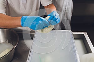 Artisan cheesemaker cuts the mozzarella with hands.