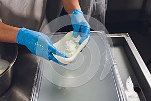 Artisan cheesemaker cuts the mozzarella with hands.