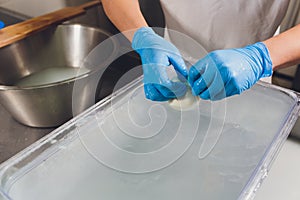 Artisan cheesemaker cuts the mozzarella with hands.