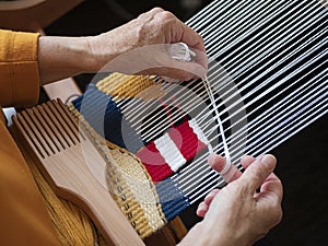 Artisan is creating a bright tapestry with lighthouse using yarn and weft beater. Handloom weaving