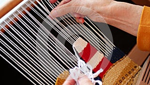 Artisan creating a bright tapestry with lighthouse using yarn and weft beater. Handloom weaving