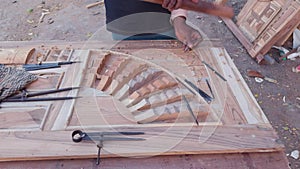Artisan hand carving intricate patterns on wooden panel with chisel showcasing craftsmanship and manual woodworking skills