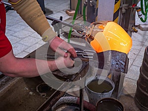 Artisan hands forming the red malleable glass on glassblower pipe