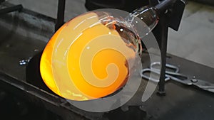 Artisan hands working with hot malleable glass on glassblower whistle. Traditional glass shaping  technique. Handmade glass studi