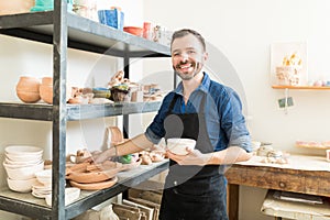 Artisan Holding Clay Bowl By Shelves In Pottery Workshop