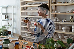 Artisan tattooed girl drink coffee and looking at tasty bun lustily in art studio during break