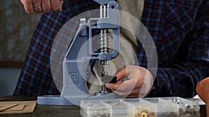 An artisan uses a press to install metal fittings. He fixes the part with the clincher in the tool and lowers the handle