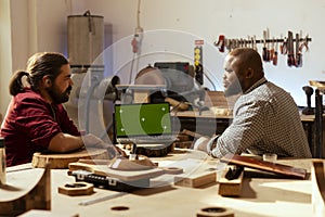 Artisans in studio comparing wood piece with blueprint on mockup laptop