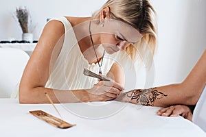 Artist applying floral henna tattoo on women hands, design for beauty