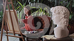 Artist in an art studio with plants - young pretty woman drawing a greek head sculpture