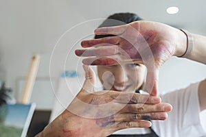 The artist creates a frame with her hands soiled with watercolor paints.