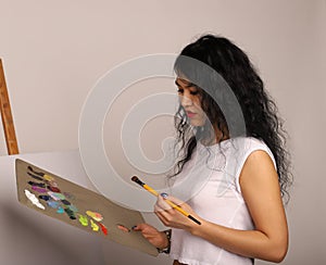 The artist at the easel paints a picture. Attractive girl with a brush paints. A blank canvas for a new painting and an artist