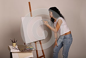 The artist at the easel paints a picture. Attractive girl with a brush paints. A blank canvas for a new painting and an artist