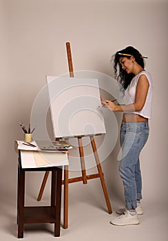 The artist at the easel paints a picture. Attractive girl with a brush paints. A blank canvas for a new painting and an artist