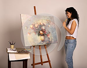 The artist at the easel paints a picture. Attractive girl with a brush paints. Oil painting, roses in a vase on canvas. Palette