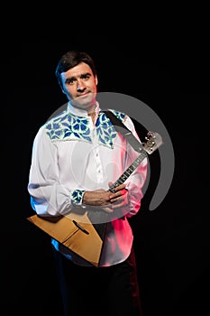 Artist musician A brunette man in a white and blue pattern folk shirt plays a balalaika