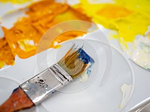 Artist paint brush on white plastic artist palette with yellow acrylic colour