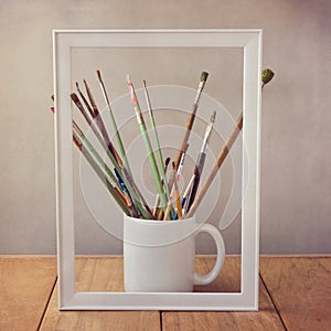 Artist painting brushes on wooden table with picture frame