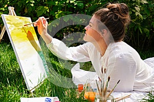 Artist painting on the easel outdoors in the garden. Open air outdoor art workshop. Draw on the canvas with brush and