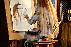 Artist painting on easel in studio. Girl paints portrait of woman with brush.